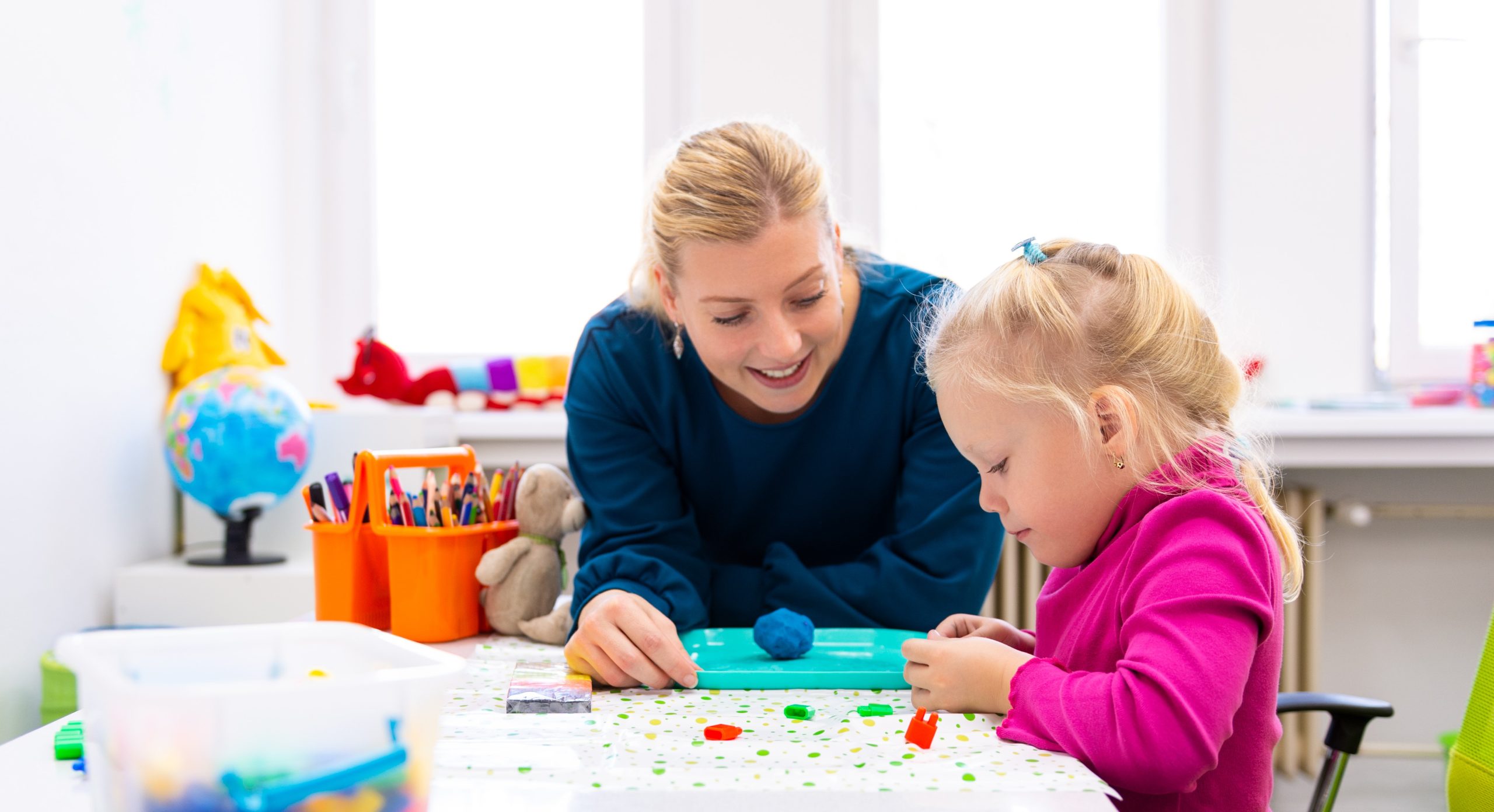 Toddler girl in child occupational therapy session doing sensory playful exercises with her therapist.